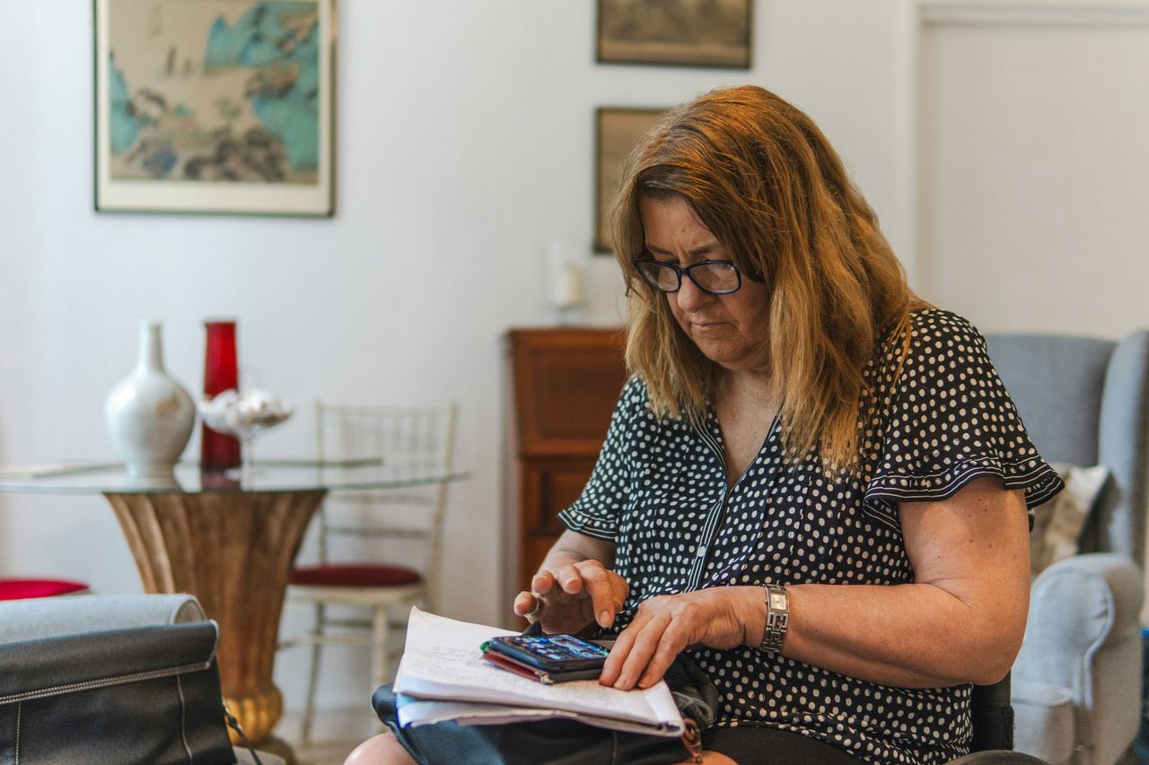 Mulher conferindo papéis numa mesa com uma calculadora na mão